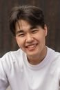 Cheerful young Asian male with dimple on cheek in white t shirt smiling and looking at camera on sunny day