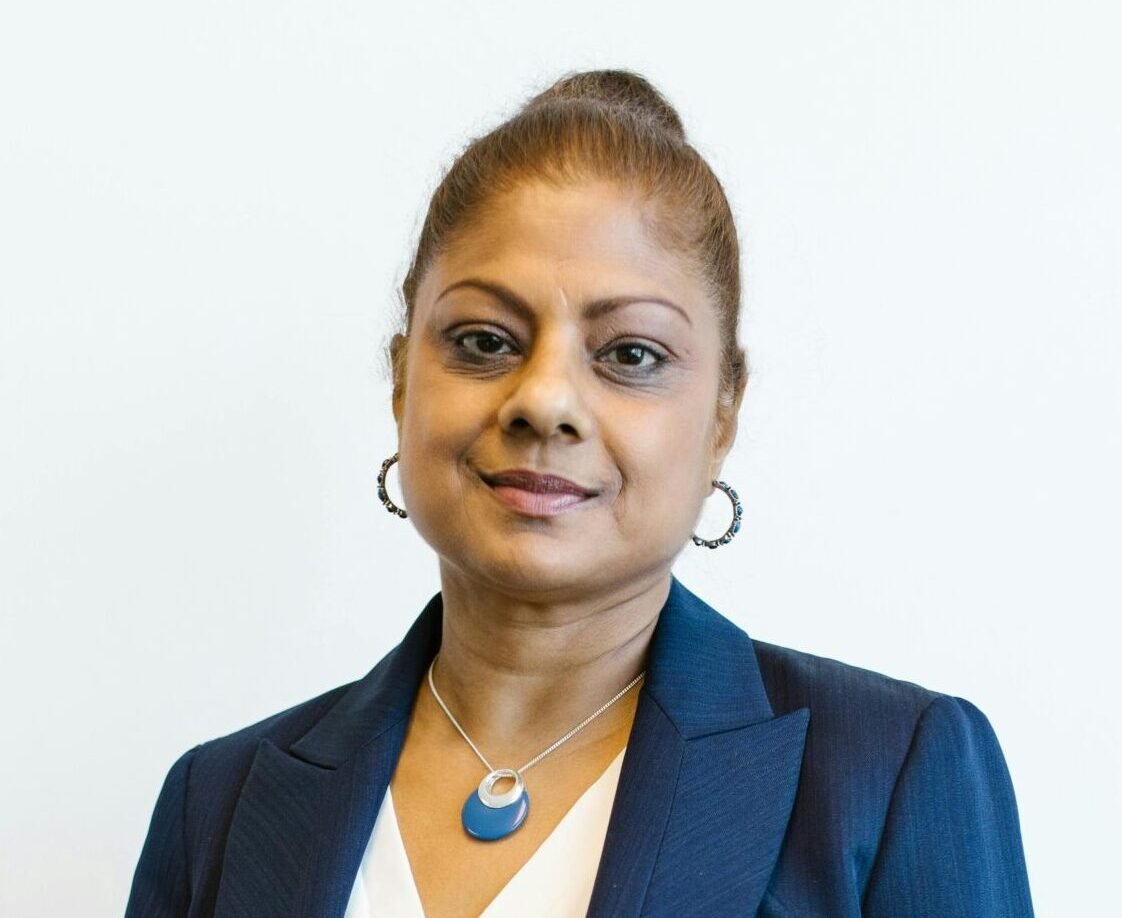 Confident woman in business attire smiling against a plain background.